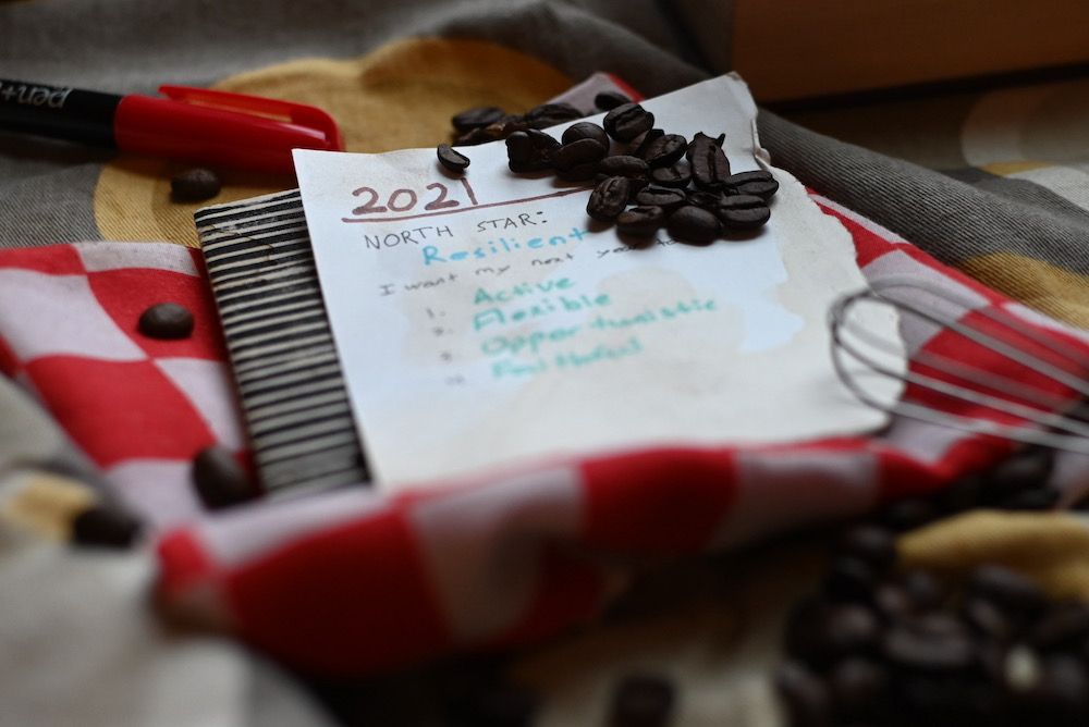 Wrinkled and stained paper with 2021 goals on it, surrounded by coffee beans and a marker